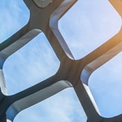 Geometric architectural structure against a bright sky with sun flare symbolizing global reach in investments.