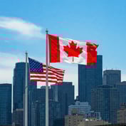 Canada and US flags against corporate city scape backdrop