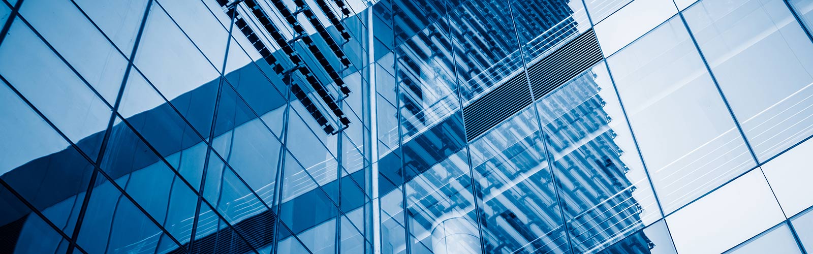 A low-angle shot of a modern skyscraper's blue, reflective glass facade, showing abstract reflections.