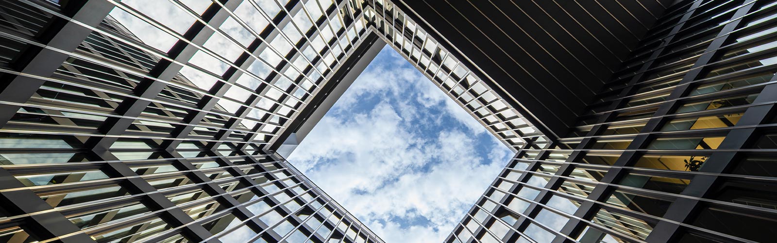 Low angle view looking up through the square atrium of a modern office building to a blue sky with white clouds