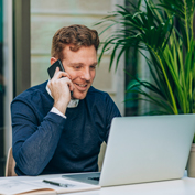 Smiling man talking on mobile phone looking at laptop on outdoor patio table